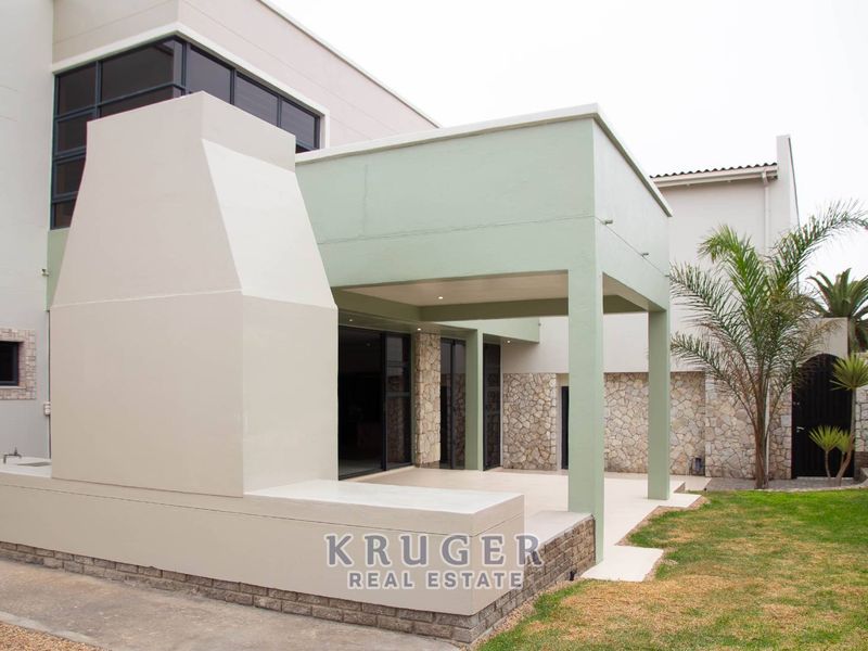 A modern covered patio featuring a built-in braai, stone cladding accents, and direct access to the garden through large sliding doors.