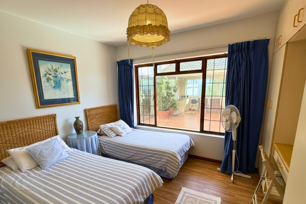A bedroom featuring built-in cabinetry, wood-look flooring, and a large window providing natural light and views of the rear patio area.