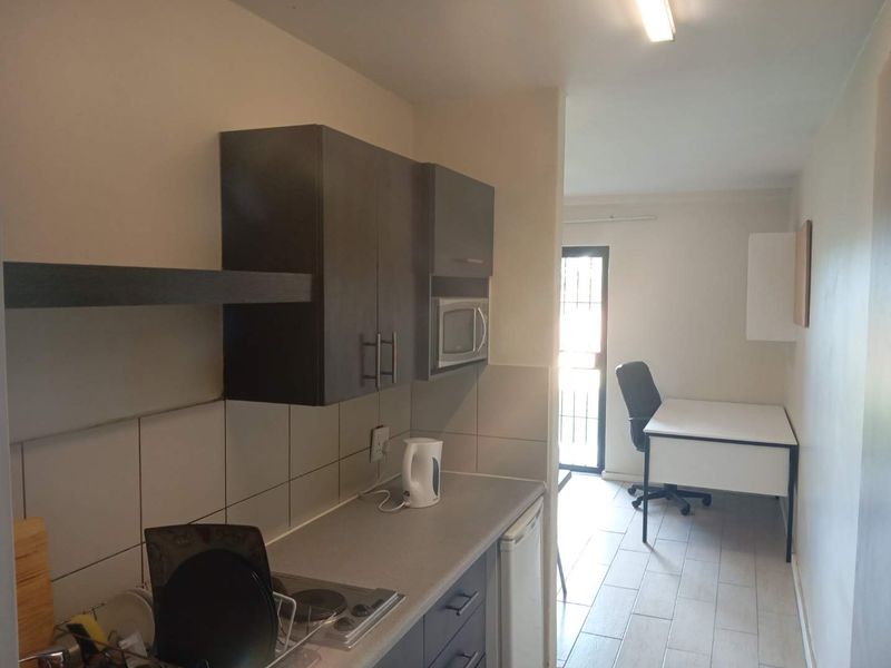 Compact kitchen featuring dark cabinetry, tiled backsplash, and built-in appliances, leading into an adjacent workspace area with tiled flooring.