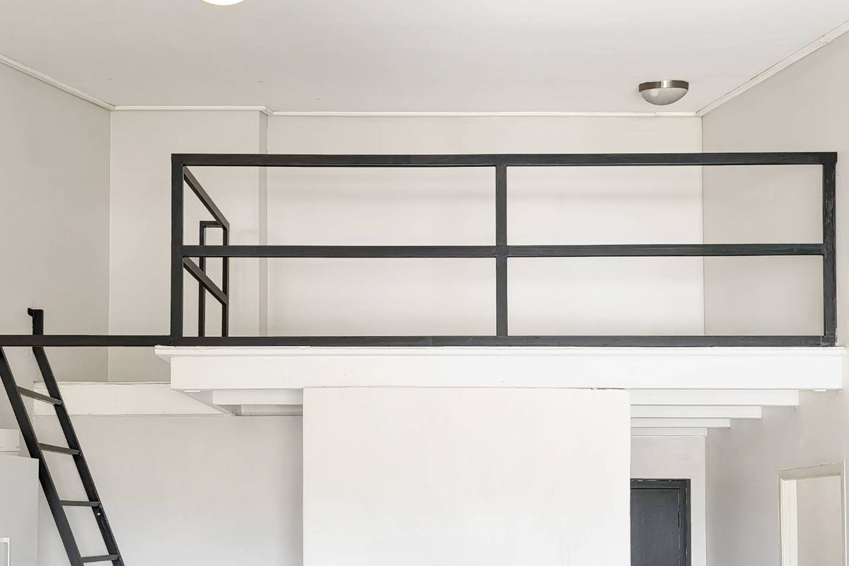 A minimalist mezzanine bedroom area featuring a black metal ladder and safety railing, providing an elevated sleeping or storage space.