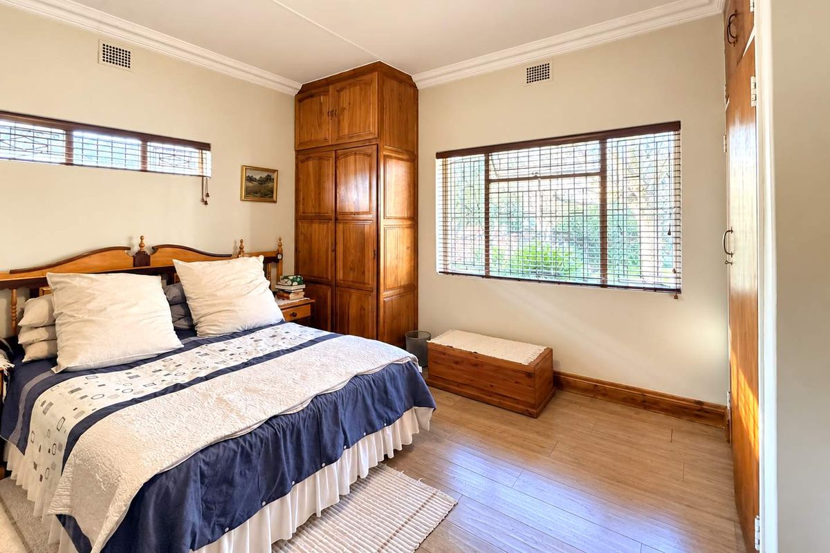 A well-lit bedroom featuring built-in wooden cabinetry, laminate flooring, and large windows with blinds, offering a functional and comfortable living space.