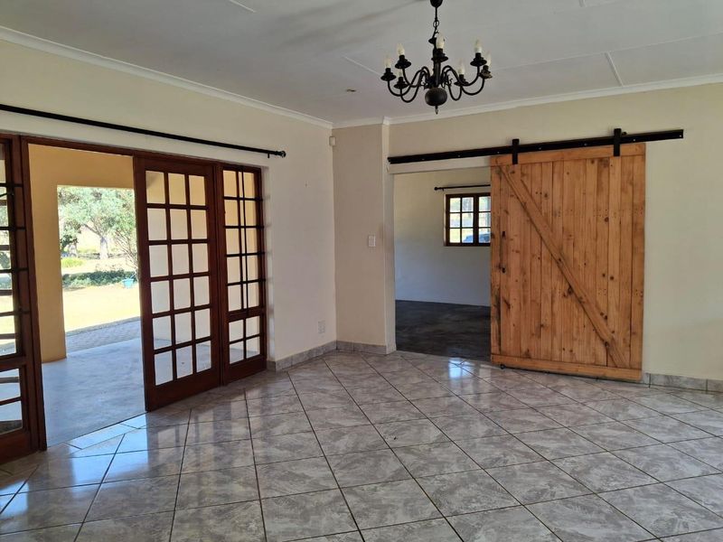 Spacious living area featuring tiled floors, a rustic sliding barn door, and large french doors opening to an outdoor patio space.