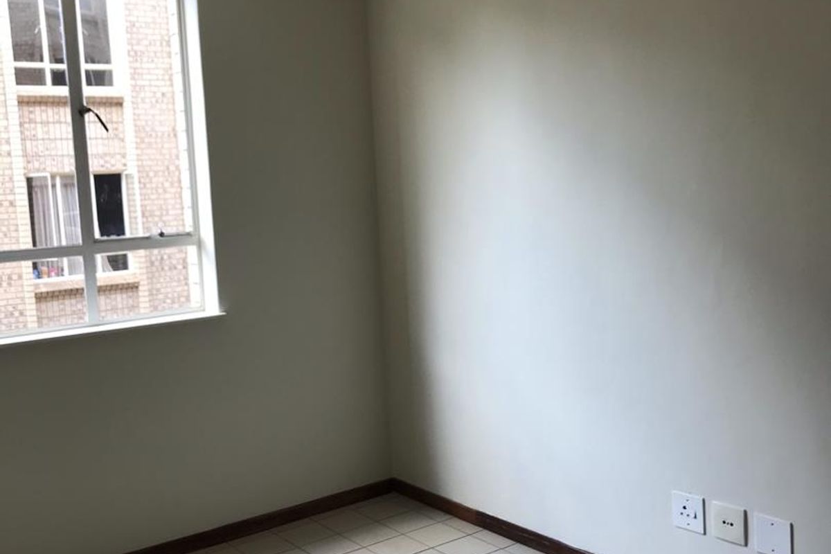 An empty bedroom featuring tiled flooring, a large window, and neutral wall finishes, ready for renovation or staging.