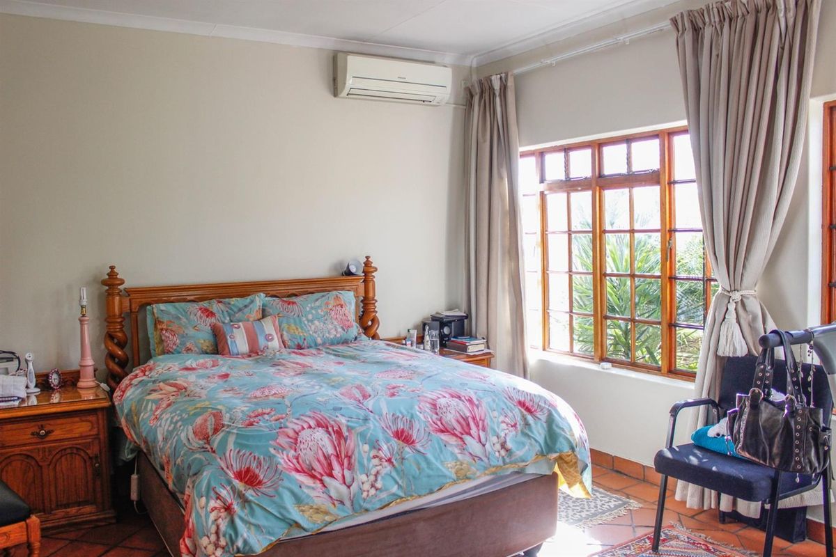 A bedroom featuring terracotta floor tiles, timber-framed windows, and a wall-mounted split-system air conditioning unit.