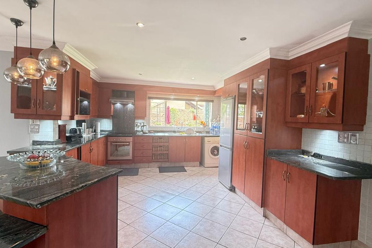 Spacious kitchen featuring warm-toned wooden cabinetry, dark granite countertops, tiled flooring, and integrated appliances, offering a functional and classic culinary workspace.