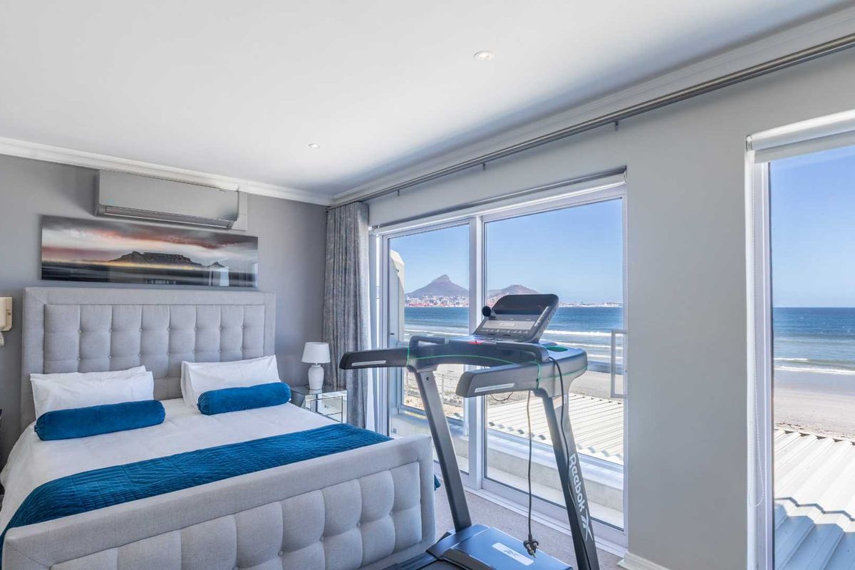 A well-maintained bedroom featuring large sliding glass doors that offer expansive ocean and mountain views, complemented by integrated air conditioning and recessed lighting.