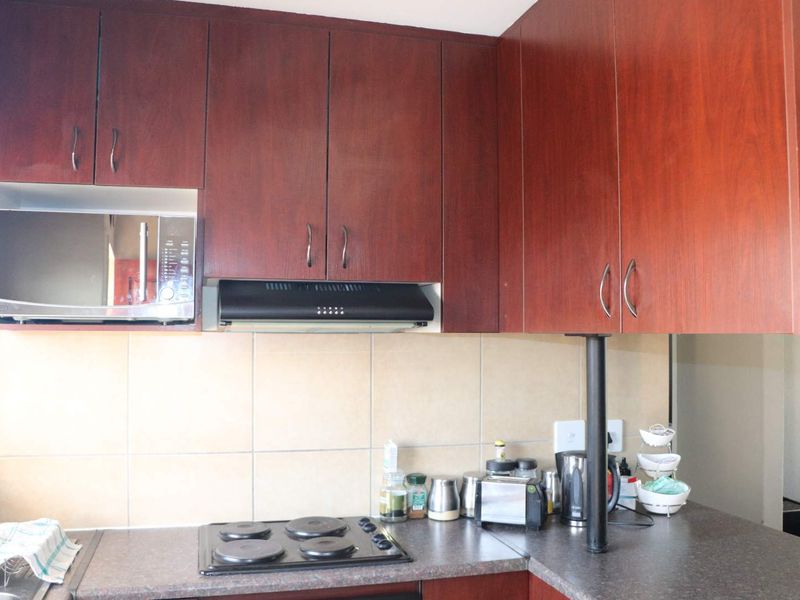 A functional kitchen featuring dark wood-look cabinetry, a built-in microwave, extractor fan, and a tiled backsplash with an electric hob.