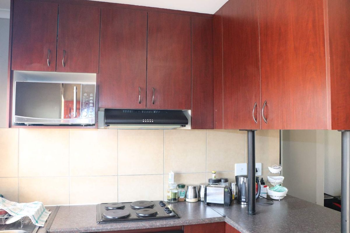 A functional kitchen featuring dark wood-look cabinetry, a built-in microwave, extractor fan, and a tiled backsplash with an electric hob.