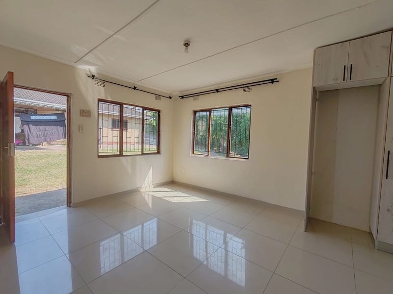 A bright, empty living room featuring tiled flooring, built-in storage cupboards, and direct access to the exterior garden area.