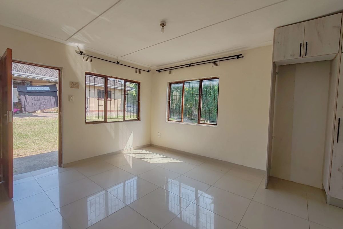 A bright, empty living room featuring tiled flooring, built-in storage cupboards, and direct access to the exterior garden area.