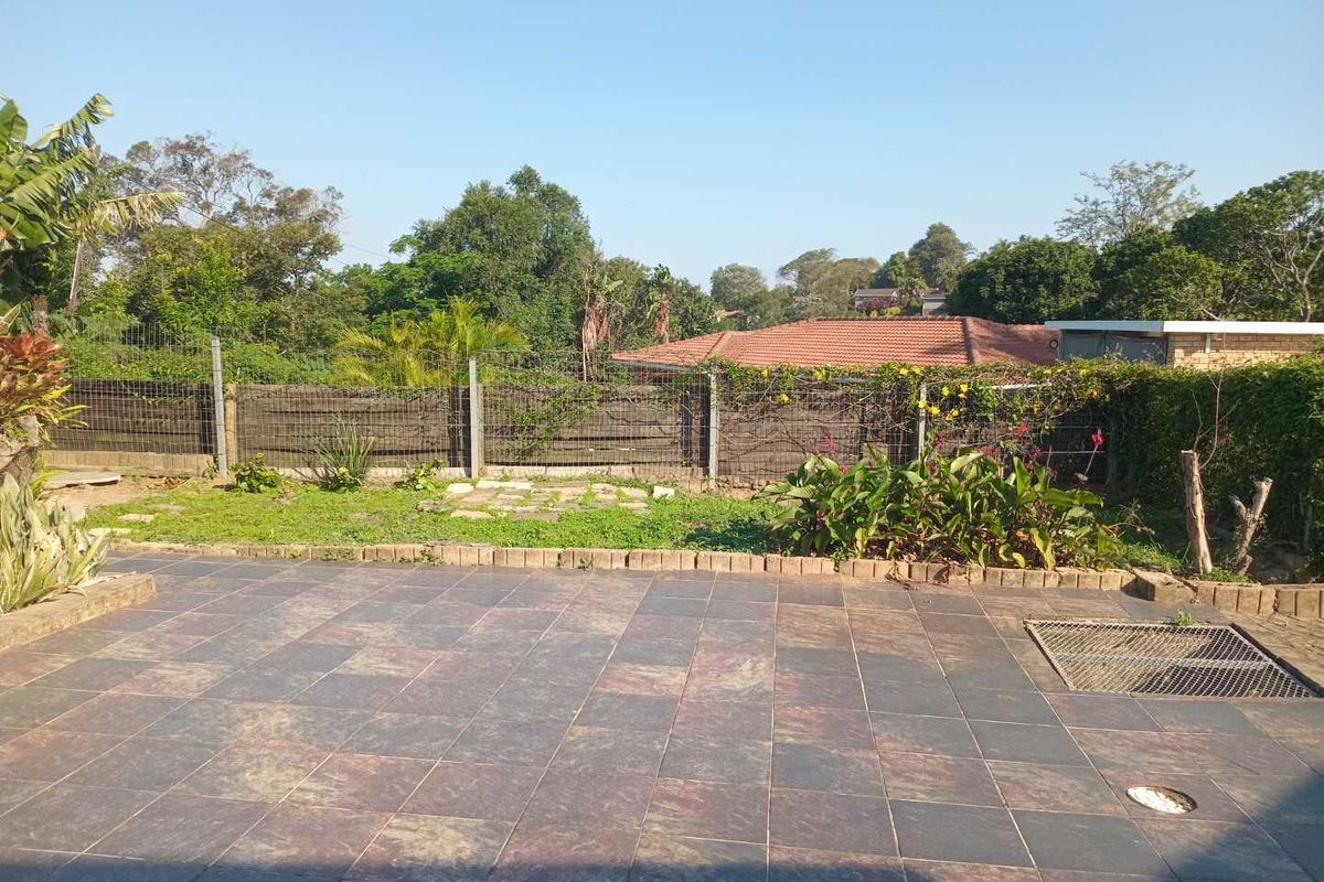A rear exterior view featuring a tiled patio area, brick edging, and a garden space enclosed by wire mesh fencing.