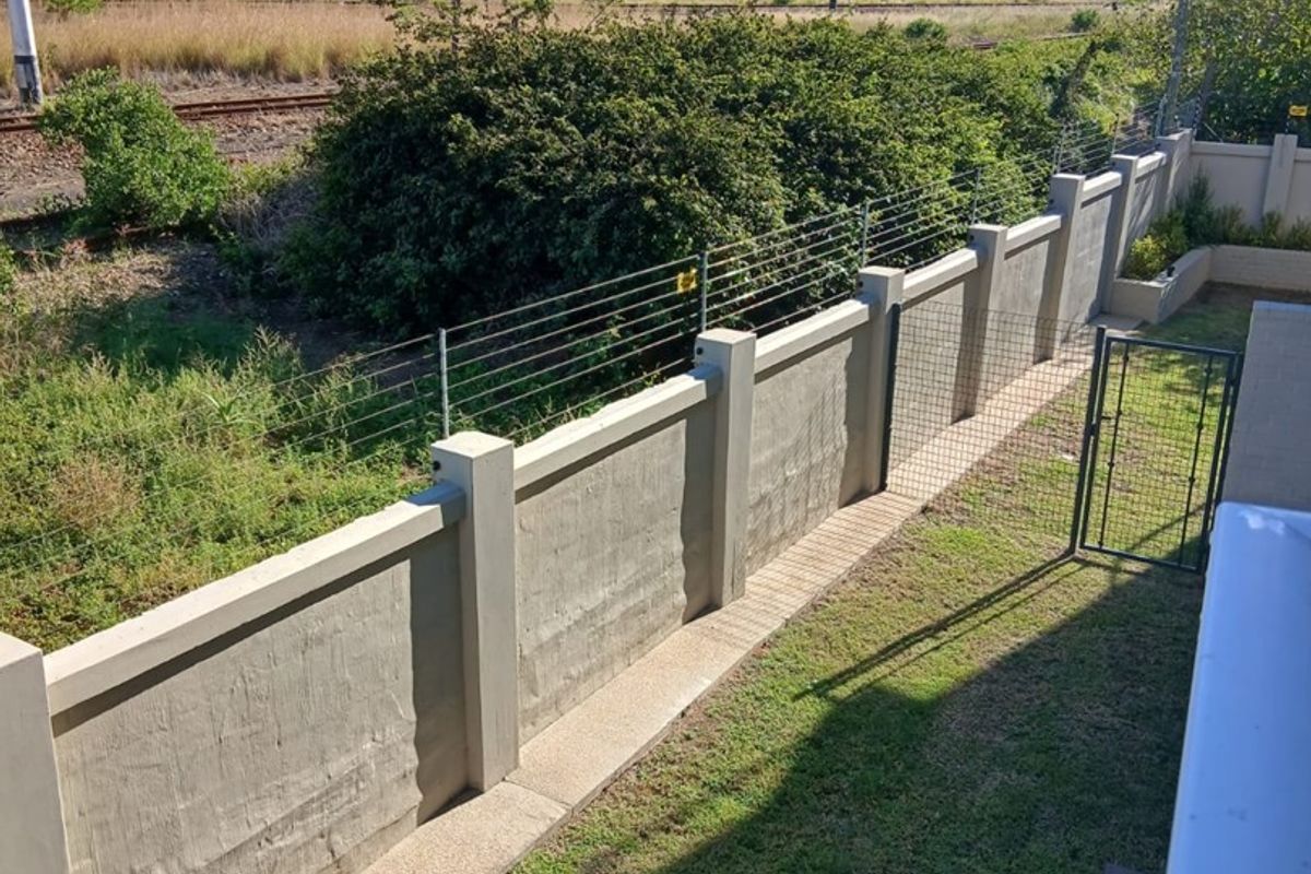 A private rear garden featuring a solid concrete boundary wall with integrated electric fencing and a paved walkway.