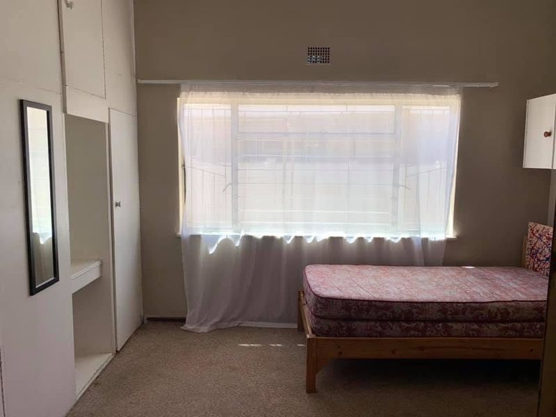 A bedroom featuring built-in cupboards, carpet flooring, and security bars on the window, offering a functional space ready for modernization.