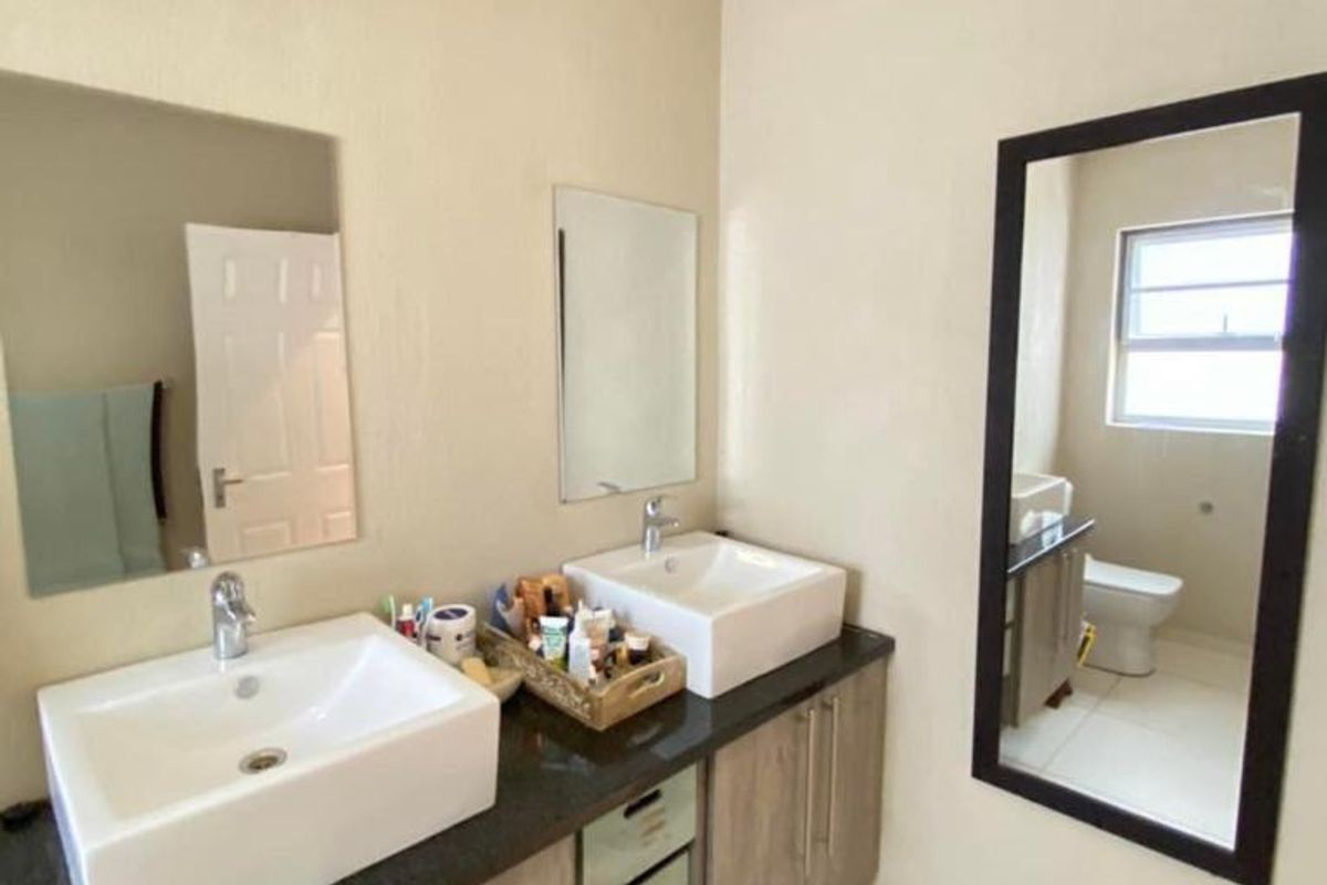 A modern bathroom featuring a double vanity with vessel sinks, granite countertop, wood-finish cabinetry, and tiled flooring.