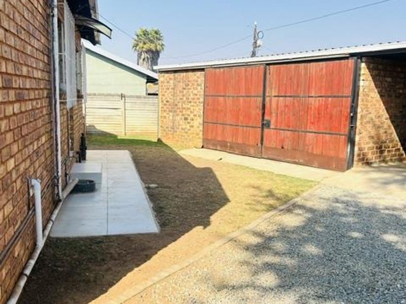 Rear exterior view showing a brick house facade, a gravel driveway, and a detached garage with wooden doors.