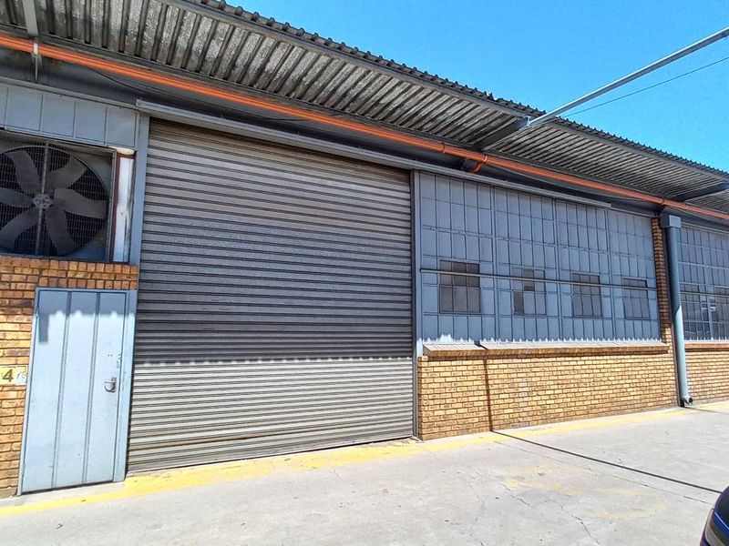 Industrial warehouse exterior featuring a large roller shutter door, face brick facade, and integrated ventilation fan, suitable for logistics or manufacturing operations.