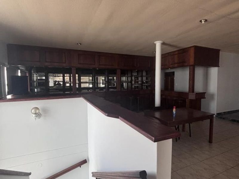 A spacious bar area featuring a built-in wooden counter, shelving, and tiled flooring, adjacent to a staircase with a wooden handrail.