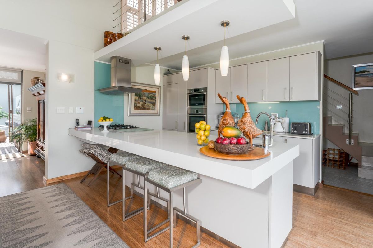 Modern kitchen featuring a large stone-topped breakfast island, integrated stainless steel appliances, sleek cabinetry, and a vibrant glass splashback.
