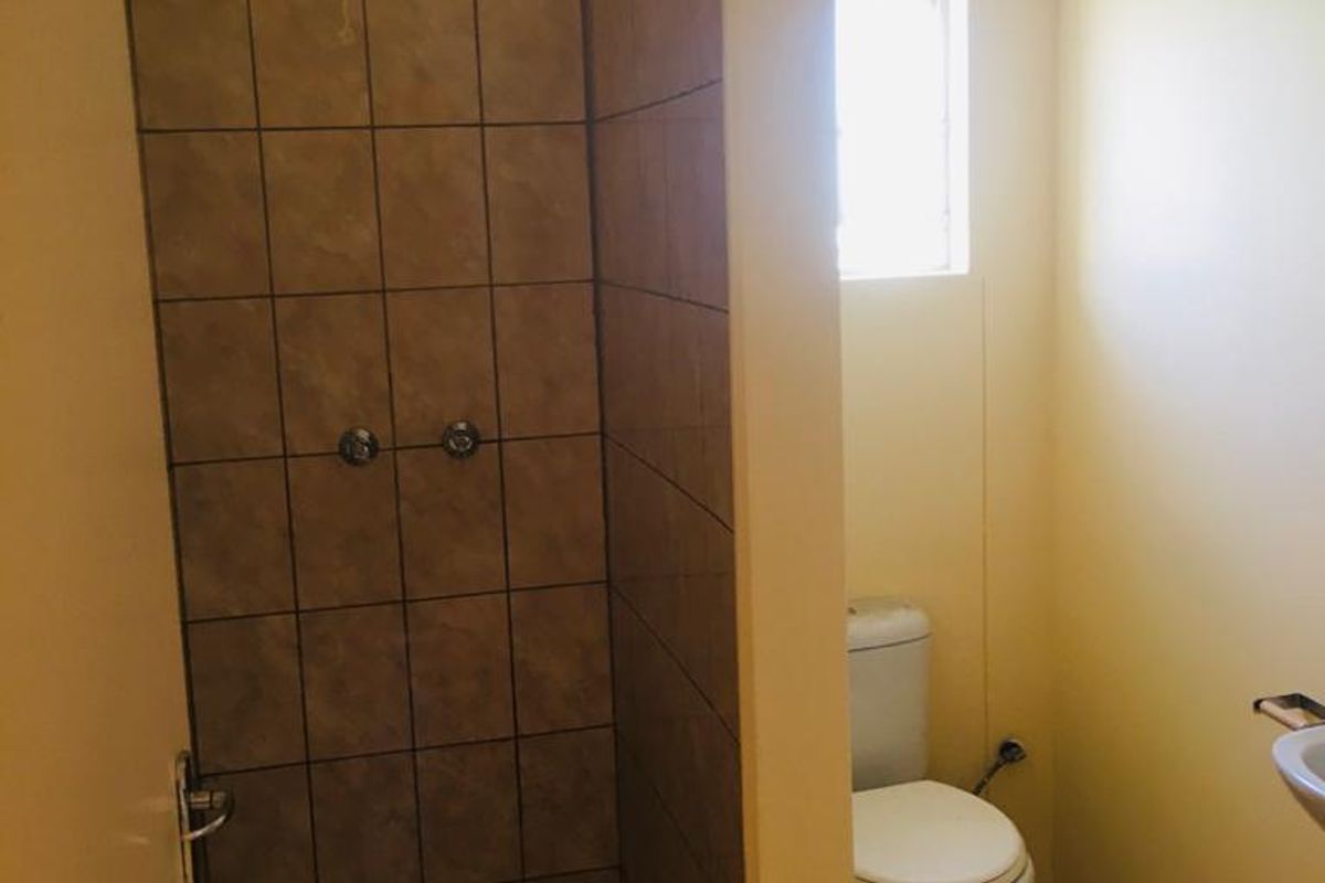 A functional bathroom featuring a tiled shower enclosure, a standard toilet, and a wall-mounted basin with yellow wall finishes.