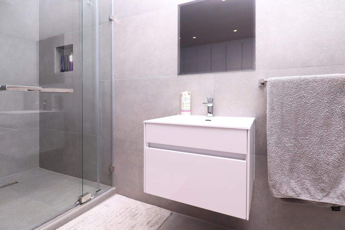 Modern bathroom featuring a wall-mounted vanity, large format grey tiling, and a glass-enclosed shower with a built-in niche.