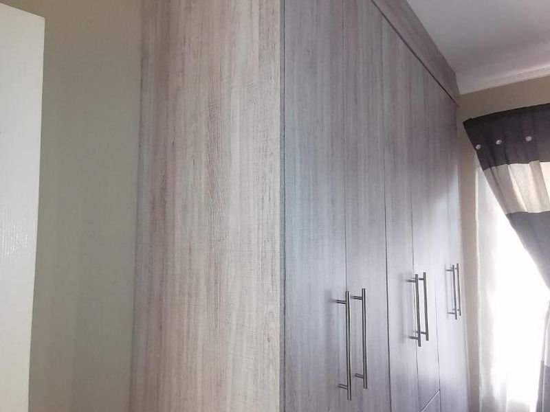 A bedroom featuring modern wood-finish built-in cupboards, tiled flooring, and decorative coving.