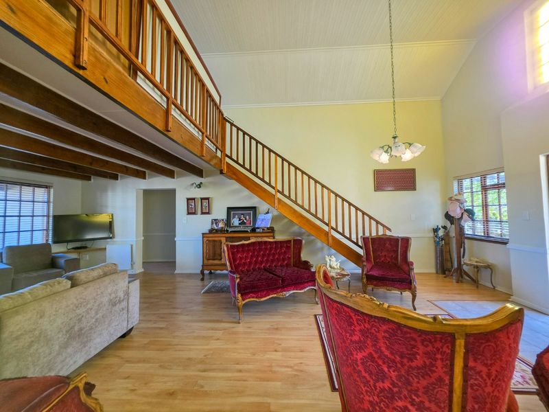 Spacious living room featuring a vaulted ceiling, exposed timber beams, and a mezzanine level with a wooden staircase.