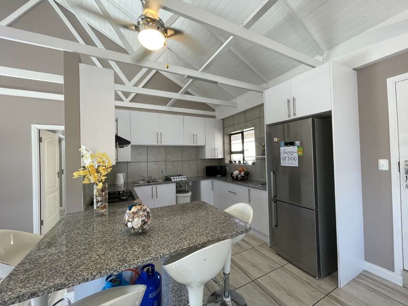 Modern kitchen featuring granite countertops, white cabinetry, gas hob, extractor fan, and exposed timber ceiling beams, creating a bright and functional cooking space.