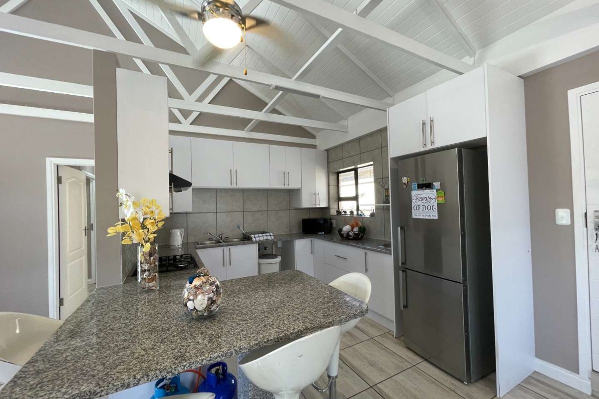 Modern kitchen featuring granite countertops, white cabinetry, gas hob, extractor fan, and exposed timber ceiling beams, creating a bright and functional cooking space.