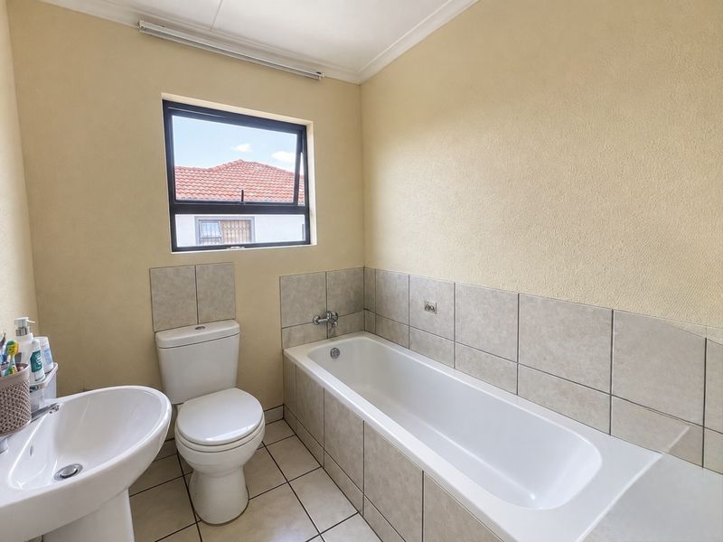 A functional bathroom featuring a pedestal basin, toilet, and a built-in bathtub with tiled splashbacks and flooring.
