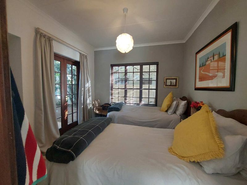 A well-lit bedroom featuring wooden French doors leading to the exterior, a window with blinds, and neutral wall finishes.