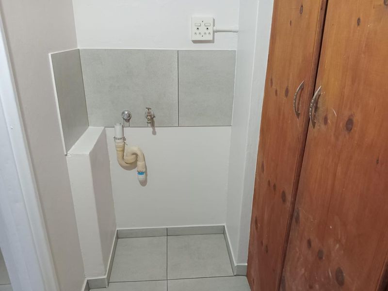 A functional laundry area featuring tiled flooring, a tiled splashback, dedicated plumbing connections, and built-in wooden cabinetry for storage.