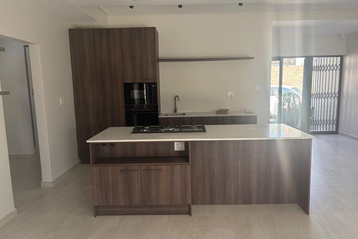 Modern kitchen featuring a central island with a gas hob, built-in oven, stone countertops, and dark wood cabinetry in an open-plan layout.