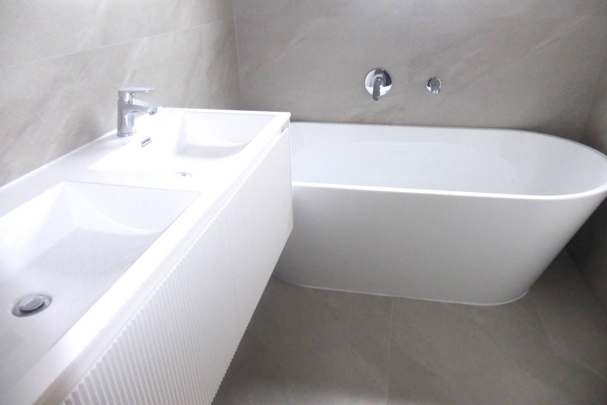 Modern bathroom featuring a sleek double vanity, a contemporary freestanding bathtub, and neutral floor-to-ceiling wall tiling.