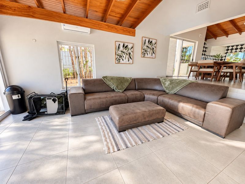 Spacious open-plan living area featuring high exposed timber beam ceilings, tiled flooring, and seamless flow to the dining space and outdoor access.