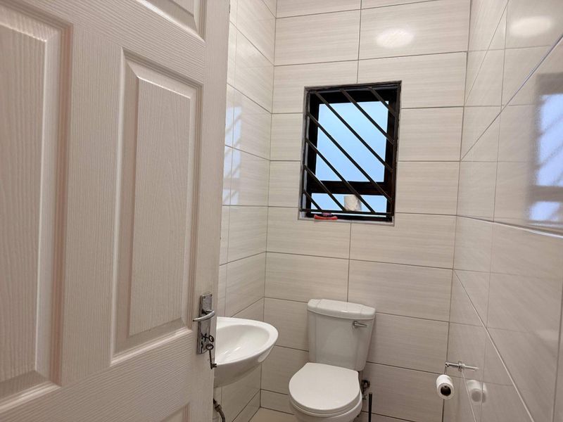A compact, modern guest bathroom featuring floor-to-ceiling ceramic tiling, a pedestal basin, and a standard toilet with security bars on the window.