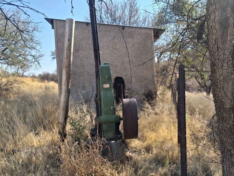 An outdoor utility structure featuring a vintage borehole pump mechanism set within a rural small holding landscape.