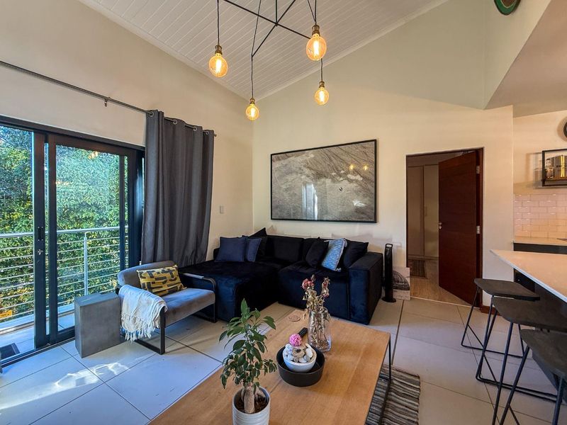 Open-plan living area featuring tiled floors, high vaulted ceilings with pendant lighting, and a seamless transition to a private balcony through sliding glass doors.