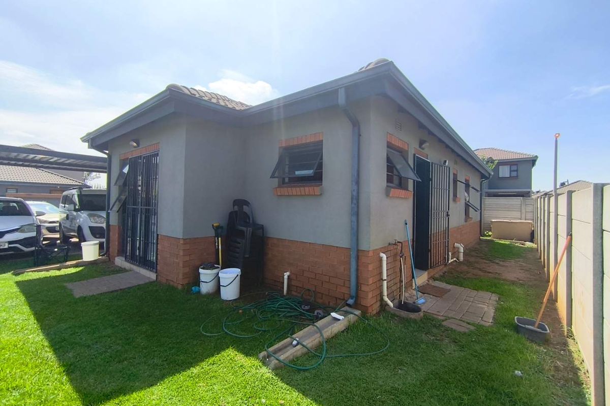 Rear view of the house featuring a combination of brick and plastered wall finishes, security gates, and a small paved area leading to the garden.