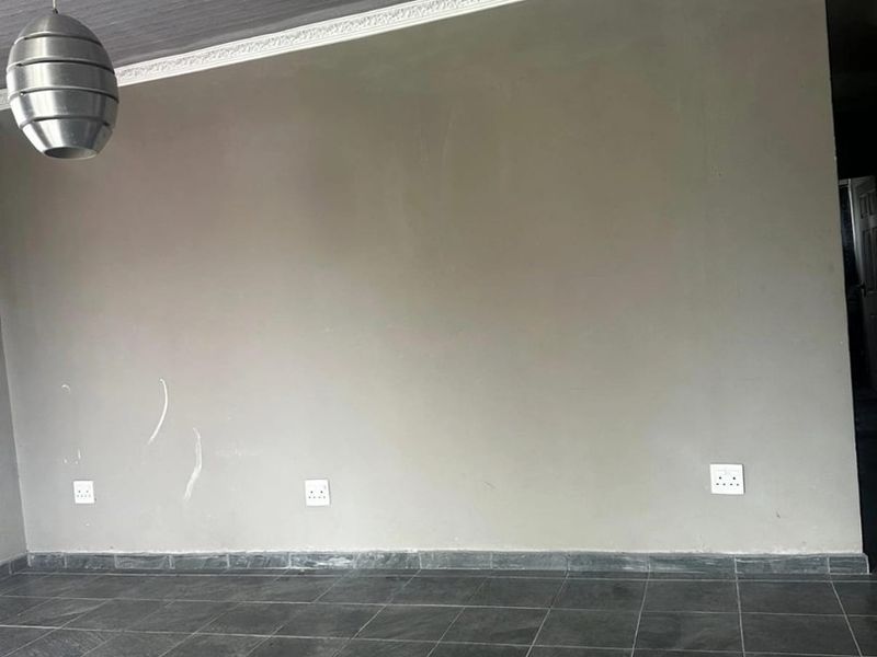 An empty living area featuring dark tiled flooring, a grey ceiling with decorative cornice, and a modern pendant light fixture.
