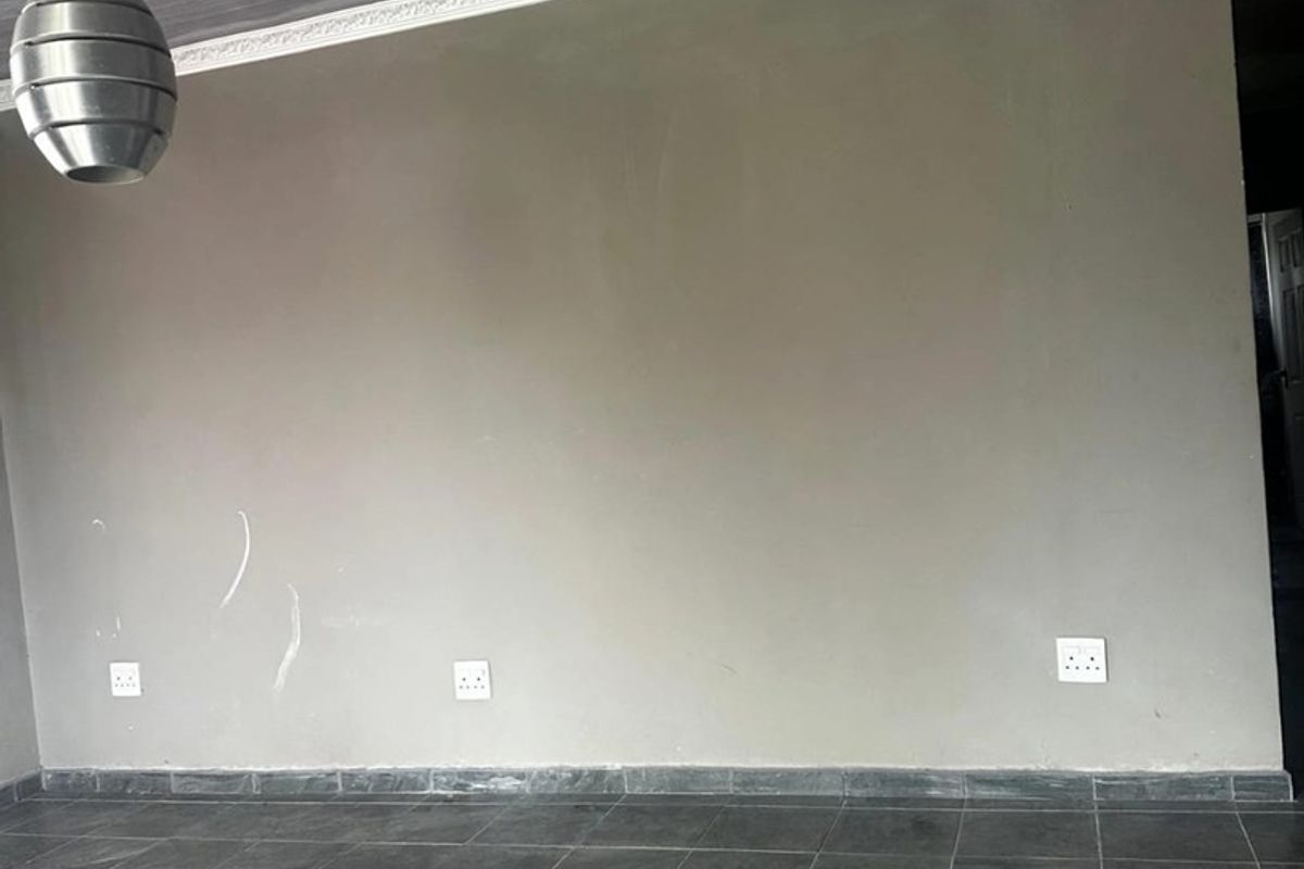 An empty living area featuring dark tiled flooring, a grey ceiling with decorative cornice, and a modern pendant light fixture.