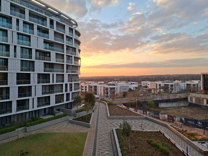 Elevated view overlooking a modern apartment complex with landscaped grounds, paved pathways, and a scenic sunset horizon.