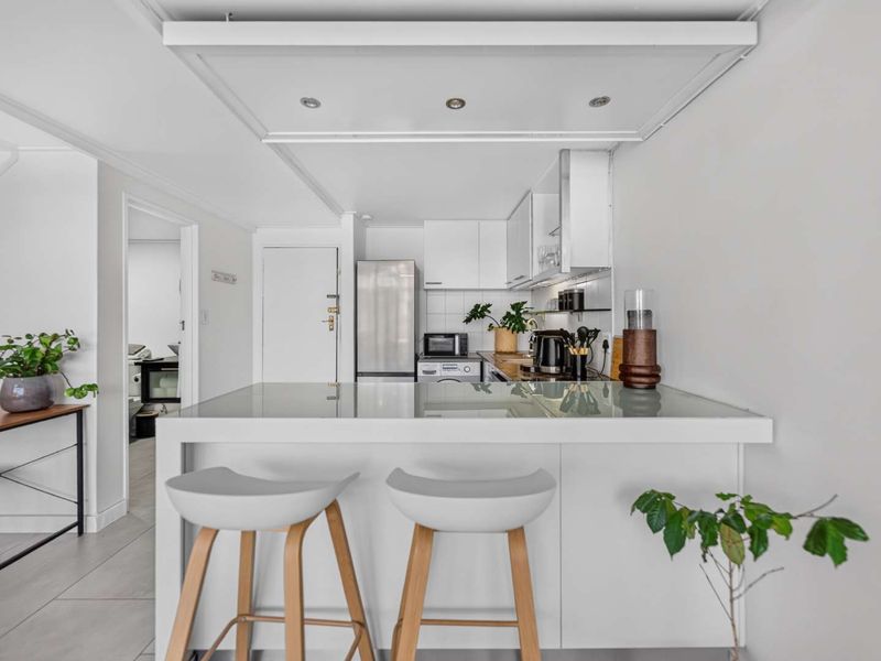 A modern, compact kitchen featuring white cabinetry, a functional island with breakfast bar seating, and recessed ceiling lighting.