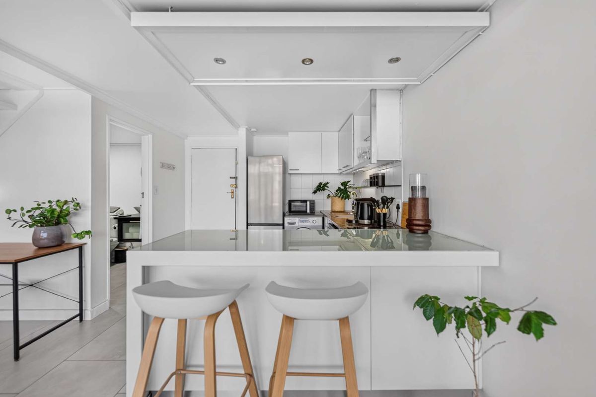 A modern, compact kitchen featuring white cabinetry, a functional island with breakfast bar seating, and recessed ceiling lighting.