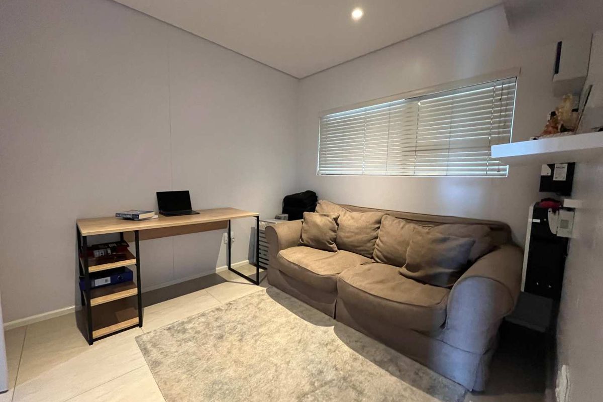 A functional bedroom or home office space featuring neutral wall finishes, tiled flooring, and horizontal window blinds.
