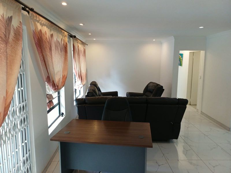 A bright living area featuring modern tiled flooring, recessed downlighting, and decorative cornicing, providing a clean and neutral foundation for interior design.