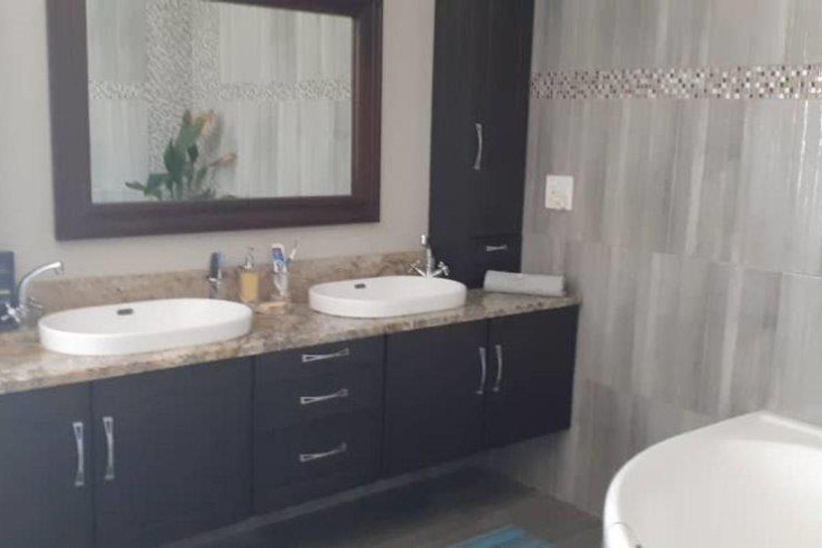 Modern bathroom featuring a double vanity with granite countertops, dark cabinetry, a large wall mirror, and a separate soaking tub with tiled wall finishes.