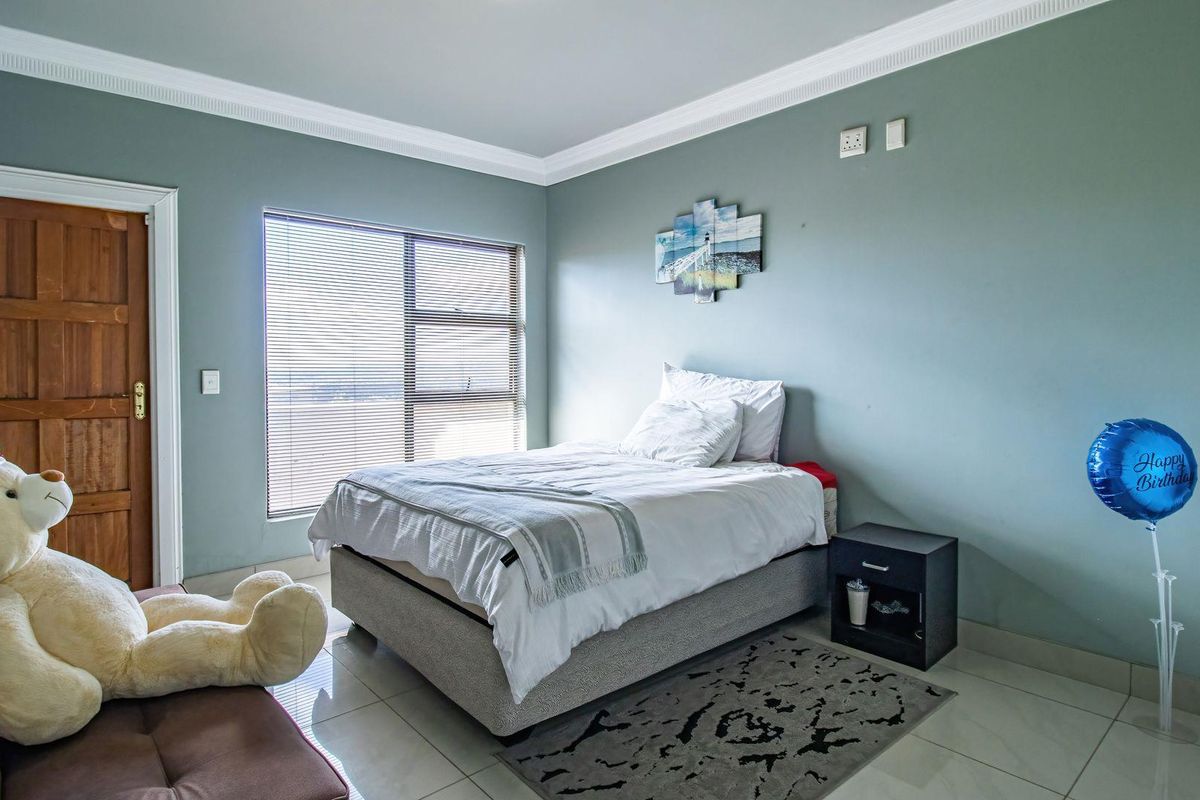 A well-lit bedroom featuring tiled flooring, crown molding, and a large window with fitted blinds.