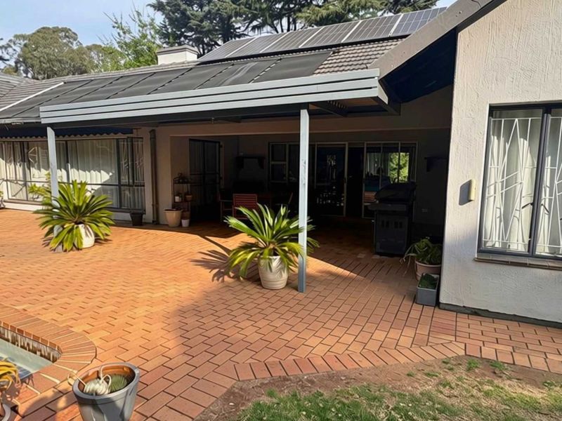A spacious covered patio area featuring brick paving, overlooking a swimming pool, with solar panels installed on the roof structure.