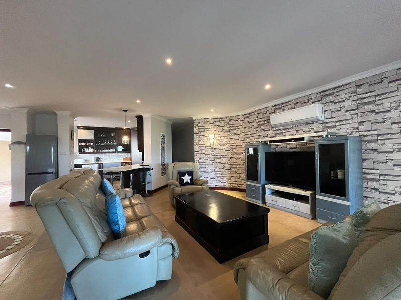 Spacious open-plan living area featuring a stone-cladding accent wall, recessed lighting, and an integrated kitchen with a breakfast island.