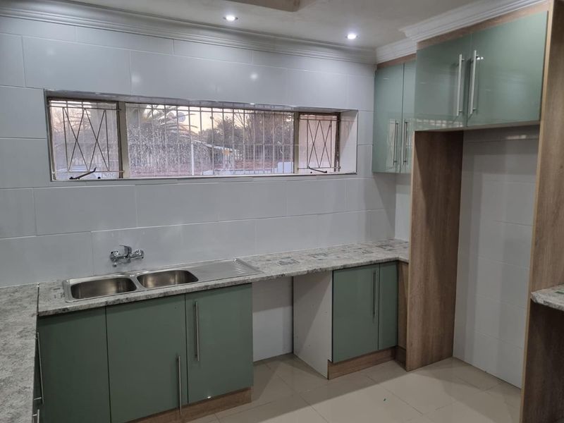 A modern, clean kitchen featuring granite countertops, double bowl sink, and ample built-in cabinetry with a neutral tiled splashback.